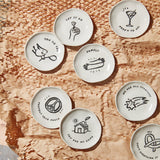Set of small ceramic plates with various designs and text on a wooden surface