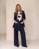 Woman wearing a navy blazer and wide-leg pants with a patterned top against a white background