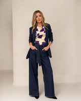 Woman wearing a navy blazer and wide-leg pants with a patterned top against a white background