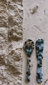 Saltist acrylic spoon and butter knife set in a blue and black tortoiseshell pattern on a stone surface.