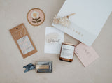 Collection of bridesmaid gifts including a box, card, and small items on a neutral background