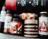 Assorted food products including spices, sauces, and a bottle of gin in a box.