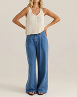 Woman wearing a cream sleeveless top and blue jeans on a plain background