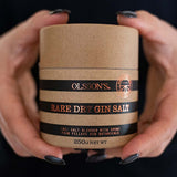 Person holding a container of Olsson's Rare Dry Gin Salt against a black background