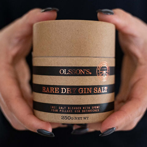 Person holding a container of Olsson's Rare Dry Gin Salt against a black background
