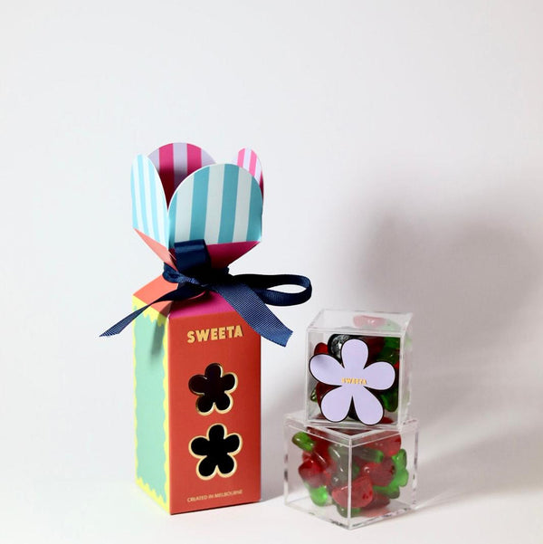 Colorful gift box with a striped ribbon and small transparent container with flowers on a white background