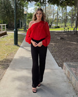 Woman wearing high-waisted black textured jersey pants with a straight-cut silhouette and a red one-shoulder top.