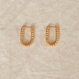 Gold chain hoop earrings on a beige fabric background