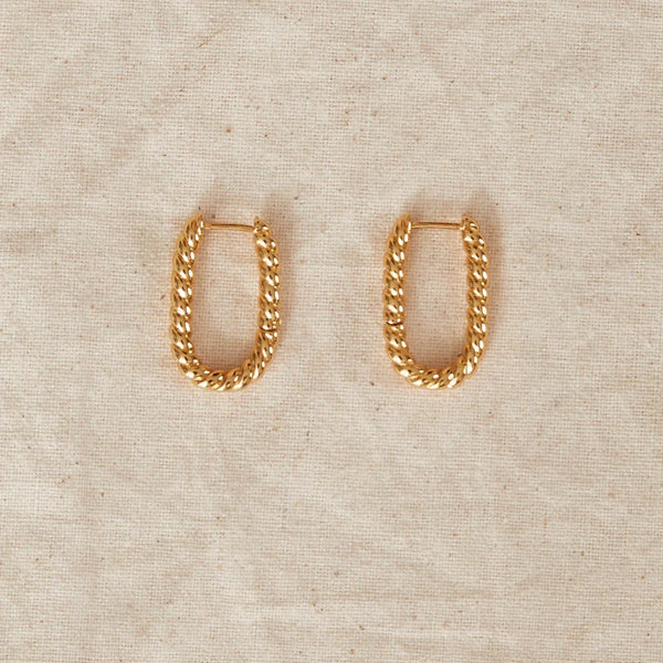Gold chain hoop earrings on a beige fabric background
