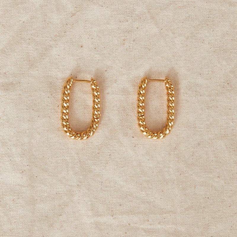 Gold chain hoop earrings on a beige fabric background