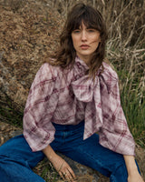 Orchid plaid pussybow blouse with a relaxed silhouette, fluid fabric, and elasticated sleeves worn with blue jeans.