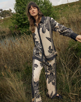 Model wearing a beige and black floral print collared shirt with contrast trim and matching trousers in a field.
