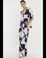 Model wearing wide-leg satin pants in cream with a bold blue and dark floral print and elastic tie waist.