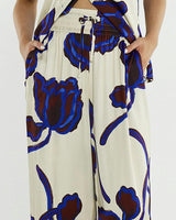 Wide-leg satin pants in cream with a blue and brown floral print, featuring an elastic waistband and side pockets.