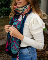 Chloe Abstract Forest scarf in black with pink, green and navy patterns and frayed edges worn over a white top.