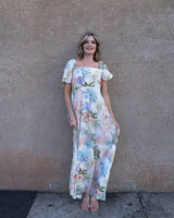 Woman wearing a floral dress standing against a plain wall.