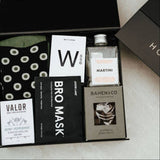 Metro Man grooming and indulgence box with Solid State Wax Cologne, martini cocktail, chocolate, Bro Mask, Valor soap, and olive spot socks