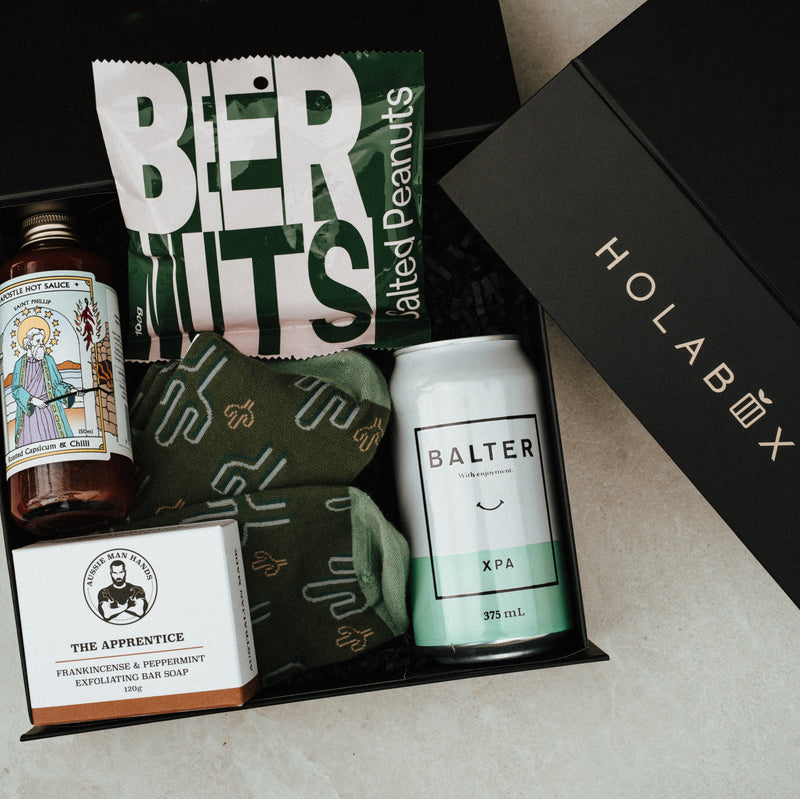 Gift box with various items including a can of Balter XPA, a bottle of hot sauce, and a bar of soap, branded 'HOLABOX'.