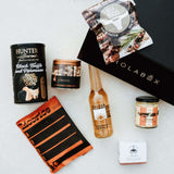 Collection of gourmet food items and a black box labeled 'HOLABOX' on a light gray background.