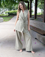 Sage green sleeveless wrap vest with notched lapels and a self-tie waist belt, worn with matching wide-leg trousers.