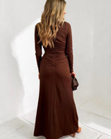 Woman wearing a long-sleeve brown jersey maxi dress with gathered back detailing, standing against a white wall.