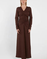 Model wearing a long-sleeve, dark brown jersey maxi dress with a V-neck and gathered front detail.