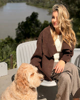 Woman wearing a brown, open-front knit Abigail cardigan jacket with ribbed trim, sitting outdoors with a golden dog.