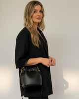 Woman wearing a black single-button linen-blend jacket with elbow-length sleeves and a matching black bucket bag.