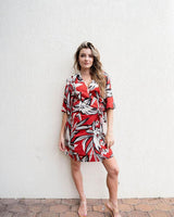 Woman wearing a red, black, and white floral print linen-blend wrap dress with short sleeves and a flattering tie waist.