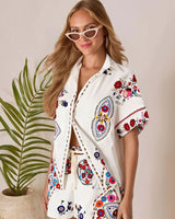 Woman wearing a white linen-blend button-up shirt and shorts set with vibrant, colorful floral embroidery.