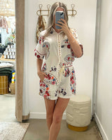 Woman wearing a white linen-blend short set with a colorful floral embroidered-style print and button-up shirt.