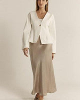Taupe midi-length bias cut satin skirt with a high-rise waist, styled with a white tailored jacket.