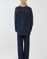Back view of a woman wearing a dark blue denim shirt with a curved hem and matching denim trousers.