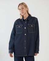 Aveline dark denim shirt with silver buttons, chest pockets, and a curved hem on a model.