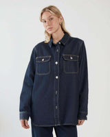 Aveline dark denim shirt with silver buttons, chest pockets, and a curved hem on a model.