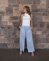 Woman wearing blue and white striped wide-leg seersucker pants with an elastic tie waist against a stone wall.