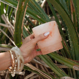 Hand-carved pink Himalayan salt Saltist margarita glass held against green foliage.