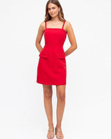 Model wearing a red Becca mini dress with a square neckline, boned bodice, and two front pockets.