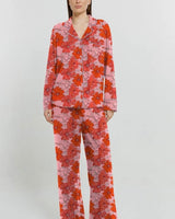 Soft pink jersey pyjama set with red floral print, button-through shirt, contrast piping, and relaxed long pants.