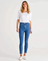 Model wearing mid-high rise blue skinny jeans with an ankle-length fit and classic button fly closure.