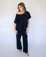 Woman wearing a navy blue cotton viscose knit top with an off-the-shoulder neckline and matching wide-leg knit pants.
