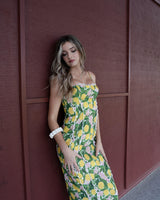 Woman wearing a lemon-print cotton-blend maxi dress with white lace trim details against a dark red wall.