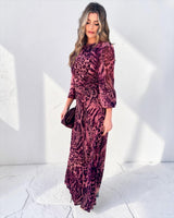 Woman wearing a flowing, cerise safari-print polyester maxi dress with long sleeves and a cinched waist.