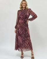 Model wearing a long-sleeve cerise safari print polyester maxi dress with a ruched waist and flowing skirt.