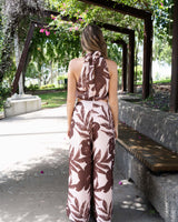 Back view of a high-neck jumpsuit in a blush and brown leaf print with a waist cut-out and tie-back closure.