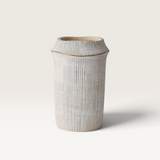 Catullo Vase in sand-toned concrete, with a tall tapered shape, fine vertical ribbing and a flared rim.