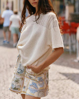 Cream-colored 100% cotton knitted tee with a round neckline and textured yoke detail, worn with patterned shorts.