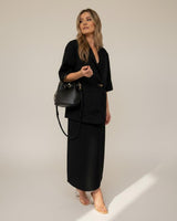 Woman wearing a relaxed black cotton-linen blend midi skirt paired with a matching blazer and black bucket bag.