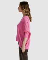 Woman wearing a bright pink Clarity Knit sweater with a boat neckline, dropped shoulders, and a hi-low hem with side splits.