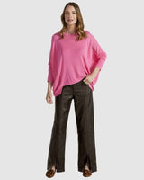Bright pink Clarity knit sweater with a boat neckline, dropped shoulders, and a hi-low hem worn with dark trousers.